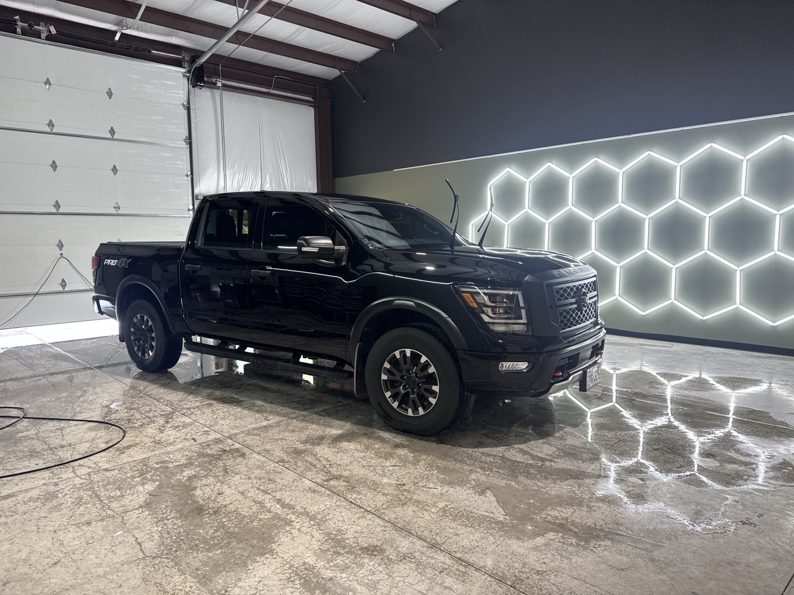 A black pickup truck with freshly finished paint parked in a detailing bay lit by hexagon LED lighting