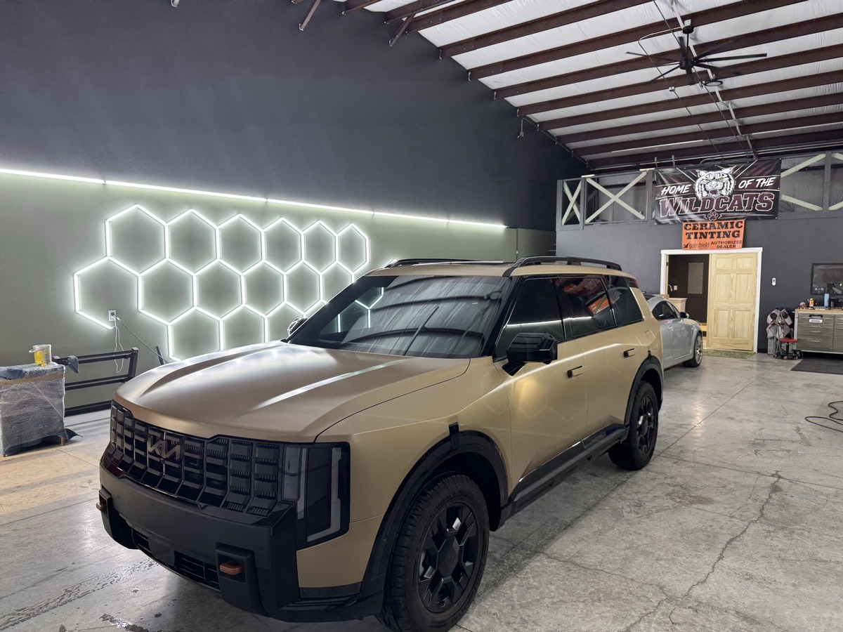 A wide view of a detailing bay with an SUV in a satin wrap under hexagon LED lighting
